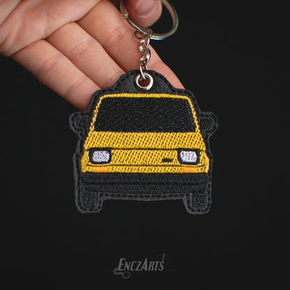 Haftowany brelok EnczArts przedstawiający żółtego Fiata 126p rękodzieło inspirowane klasykami motoryzacji.