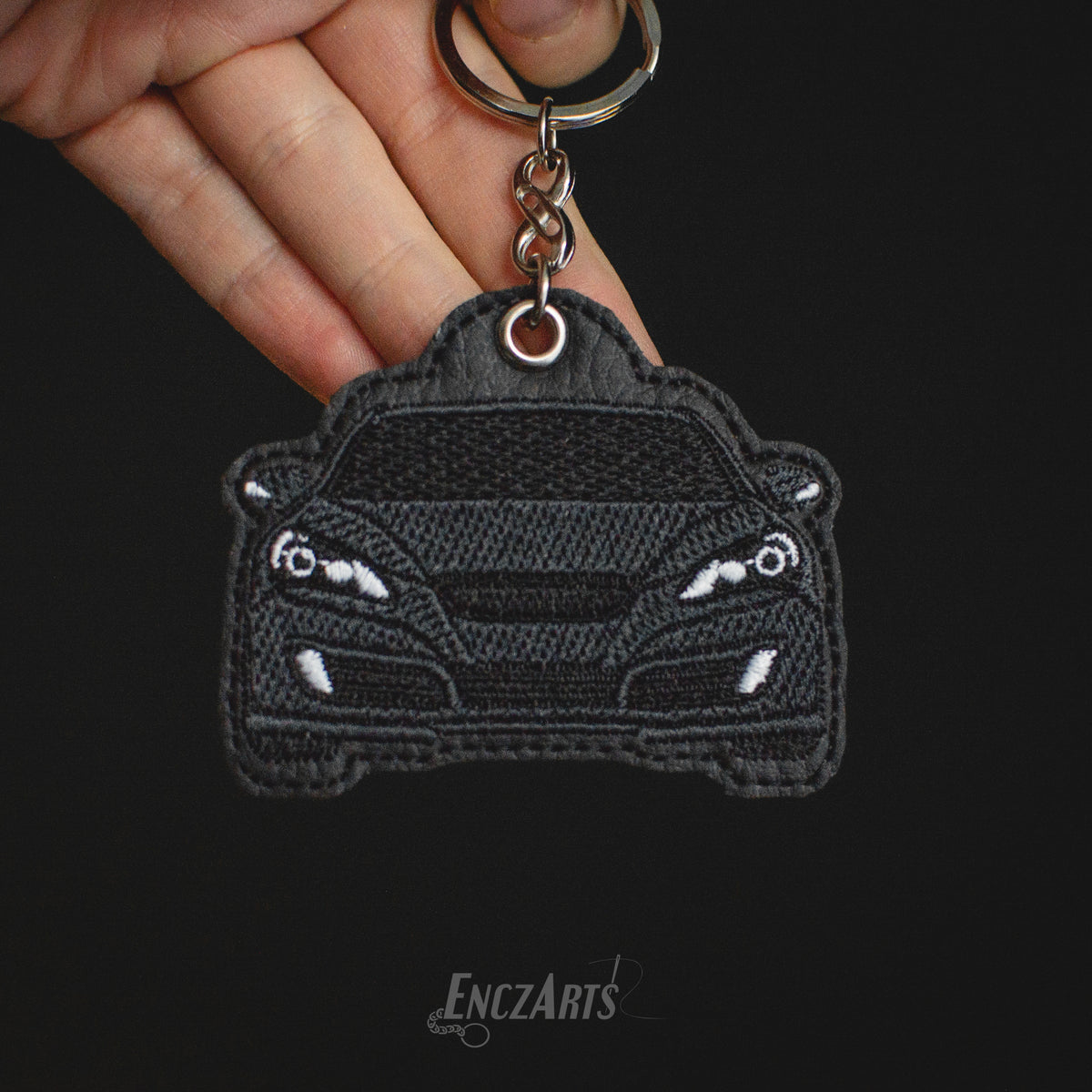 Brelok haftowany z sylwetką sportowego auta Hyundai Genesis Coupe I generacji (czarny kolor). Miniaturka samochodu na ekoskórze tapicerskiej, upominek dla miłośnika motoryzacji.
