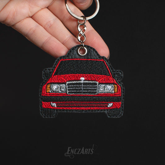 Haftowany brelok EnczArts przedstawiający czerwonego Mercedesa W124 rękodzieło inspirowane klasykami motoryzacji.