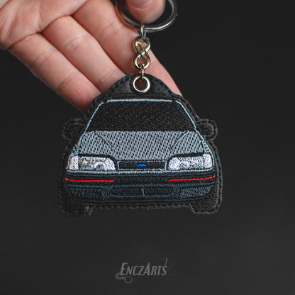 Haftowany brelok samochodowy EnczArts model Ford Sierra w kolorze srebrnym.
